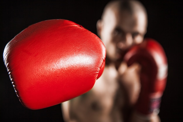 The young male athlete kickboxing on a black background