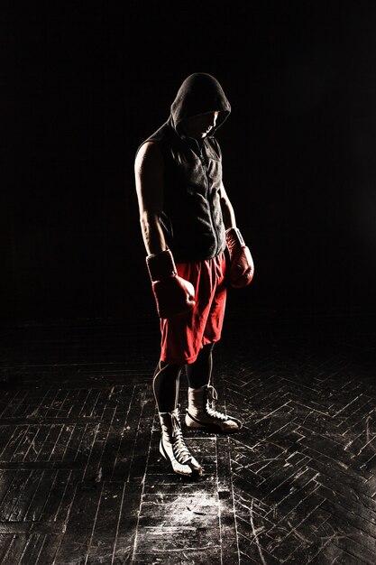 The young male athlete kickboxing standing against black background