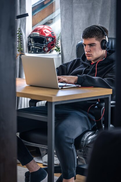 Молодой спортсмен сидит перед ноутбуком в своей комнате