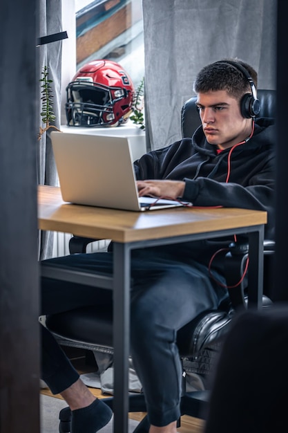 A young male athlete sits in front of a laptop in his room