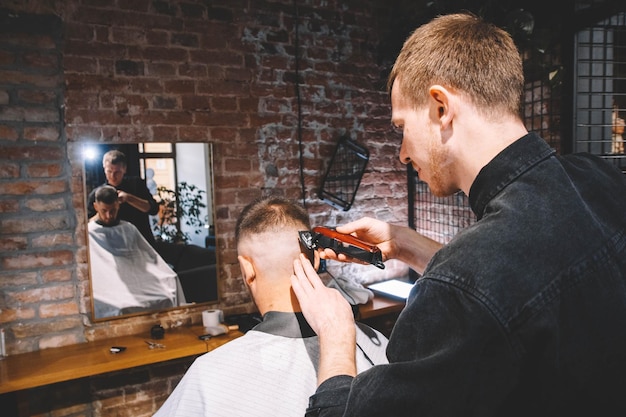 若い​男性​の​床屋​は​、​電気​トリマー​で​クライアント​の​頭​を​剃ります​。​理髪店​で​美容師​に​散髪されている​若​いひげ​を​生やした​男​。​広告​と​理髪店​の​コンセプト