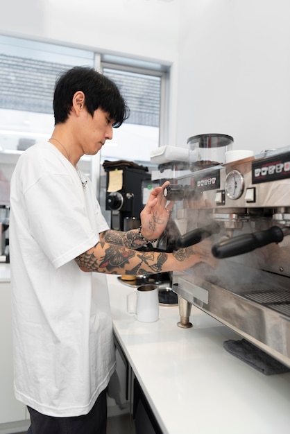 Foto gratuita giovane barista maschio con tatuaggi che usa la macchina del caffè al lavoro