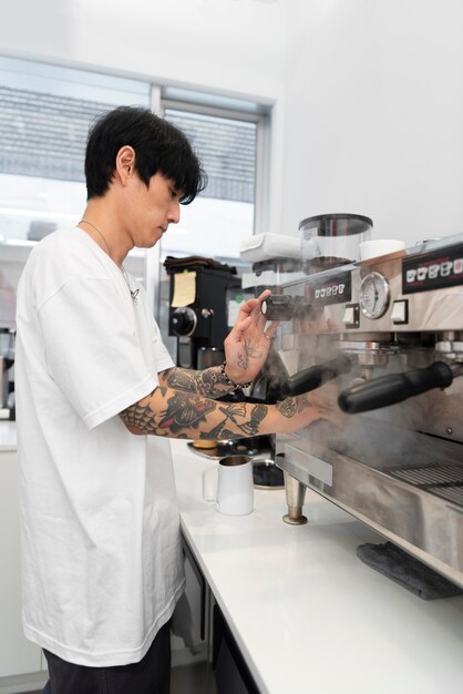 Young male barista with tattoos using the coffee machine at work