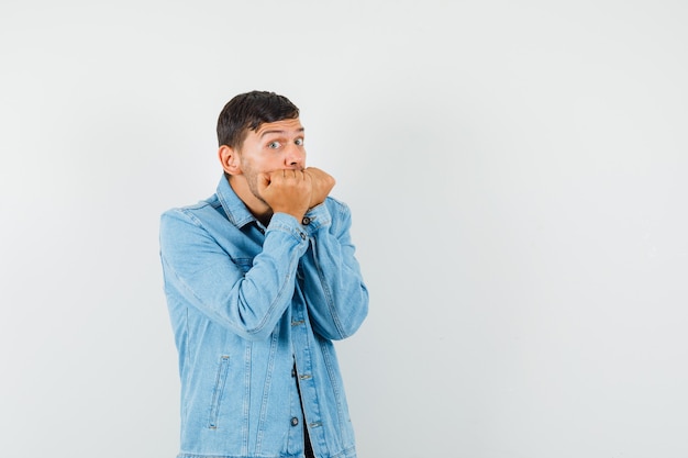 Young male biting fists emotionally in t-shirt jacket and looking terrified 