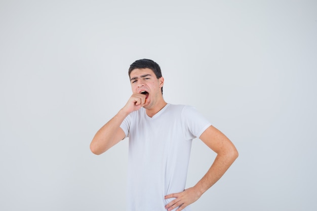 Young male biting him fist in t-shirt and looking confused , front view.