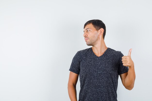 Young male in black t-shirt looking aside while showing thumb up , front view.