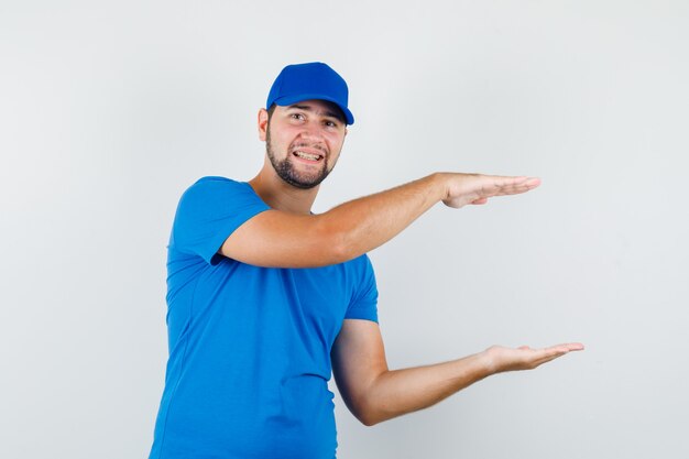 Young male in blue t-shirt and cap showing size sign and looking cheerful
