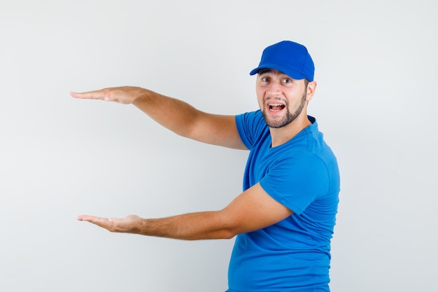 Young male in blue t-shirt and cap showing size sign and looking cheery