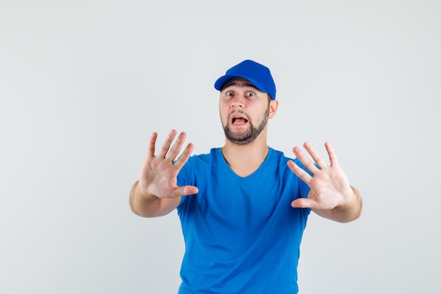 Young male in blue t-shirt and cap showing stop gesture