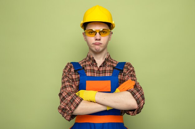 올리브 녹색 벽에 격리된 안경을 쓴 유니폼과 장갑을 끼고 있는 젊은 남성 건축업자