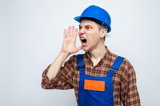 Young male builder wearing uniform isolated on white wall with copy space