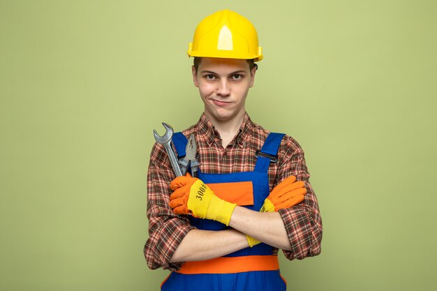 올리브 녹색 벽에 격리된 개방형 렌치를 들고 장갑을 끼고 유니폼을 입은 젊은 남성 건축업자