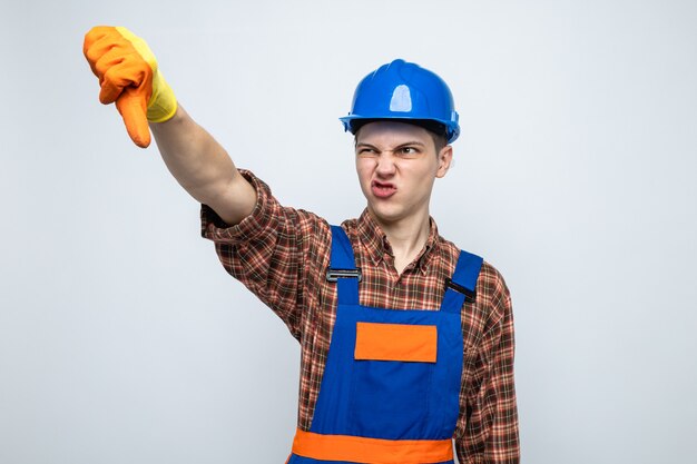 Young male builder wearing uniform with gloves isolated on white wall