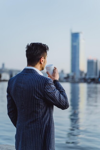 young male businessman in the city drinks morning coffee calls on smartphone