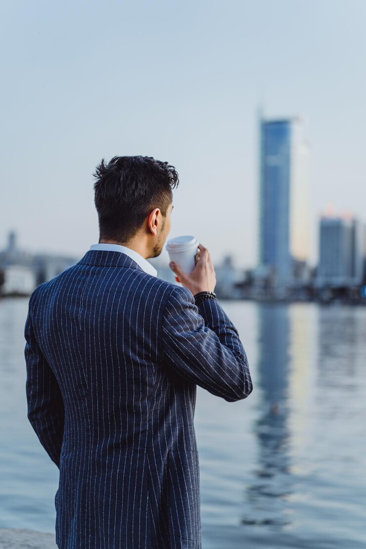 市内の若い男性ビジネスマンはスマートフォンで朝のコーヒーの呼び出しを飲みます