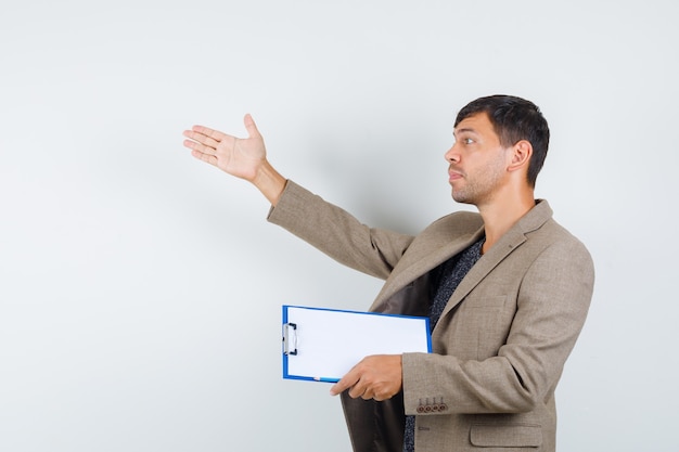 Young male calling someone while holding notebook in grayish brown jacket and looking concentrated. .