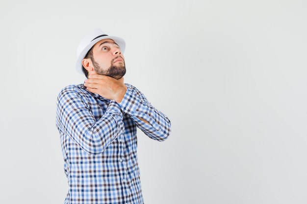 Young male in checked shirt, hat suffering from sore throat, having suffocation and looking unwell , front view.