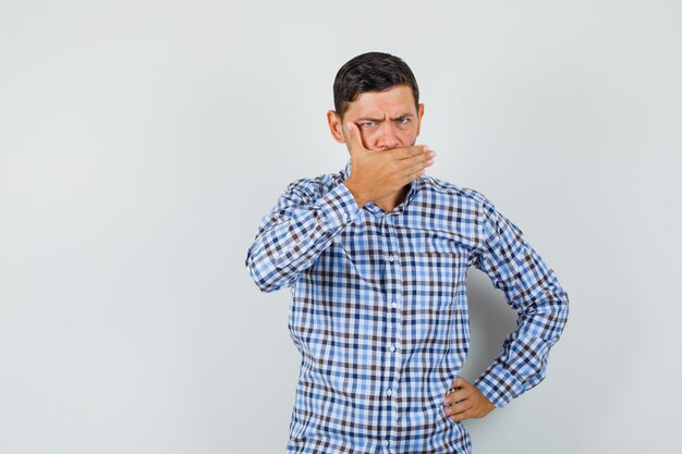 Young male in checked shirt holding hand on mouth and looking mysterious