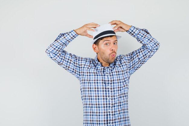 Free photo young male in checked shirt holding hands on his hat and looking puzzled