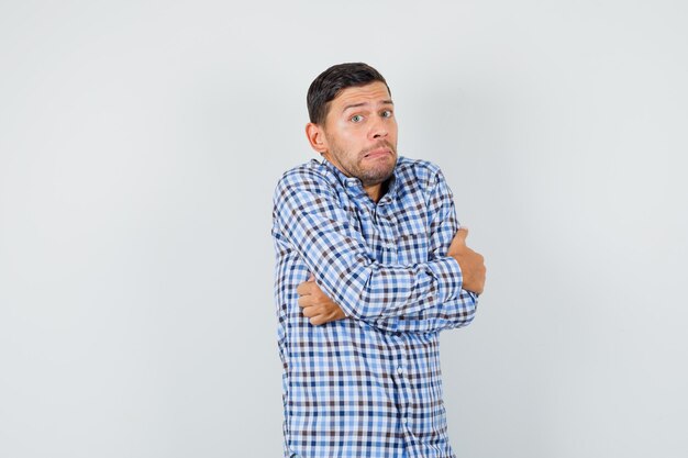 Free photo young male in checked shirt hugging himself and looking humble