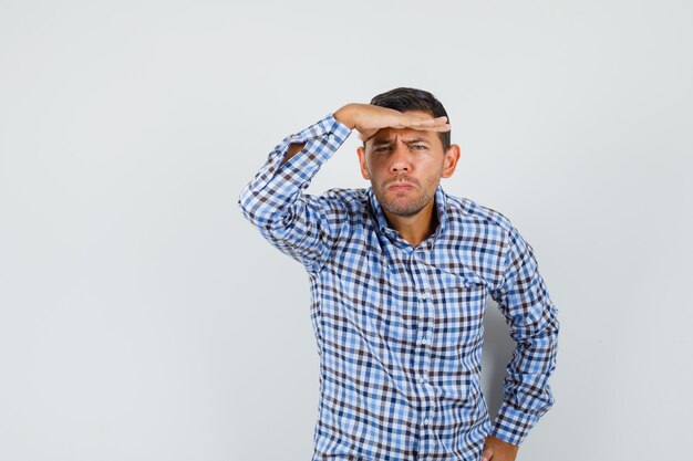 Young male in checked shirt looking far away with hand over head