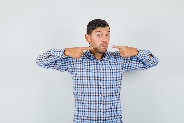 Young male in checked shirt pointing at his mouth and looking confident