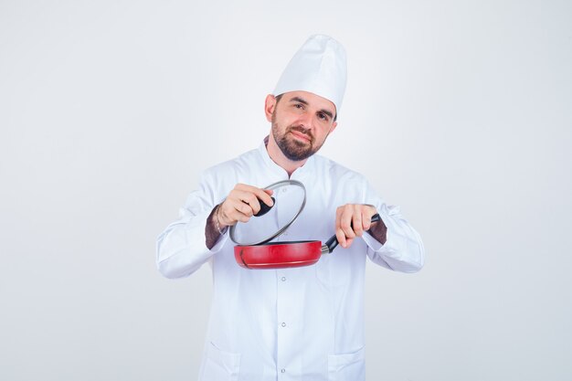 흰색 유니폼에 프라이팬에서 뚜껑을 제거하고 호기심, 전면보기를 찾고 젊은 남성 요리사.