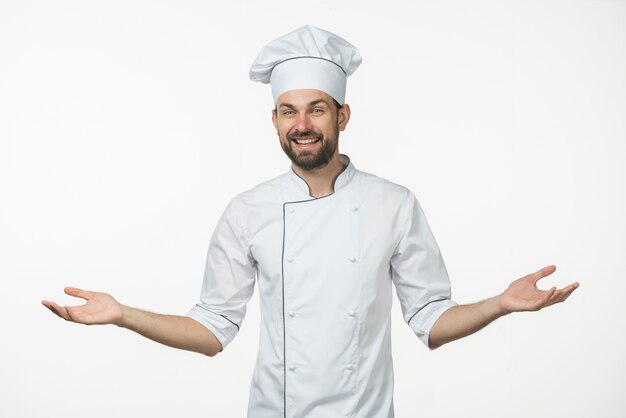 Young male chef in uniform standing against white background shrugging