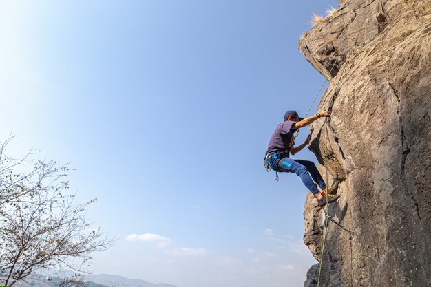 Молодой мужчина-альпинист на скалистом утесе на фоне голубого неба