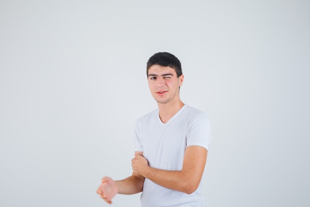 Young male closing one eye while looking at camera in t-shirt and looking funny. front view.