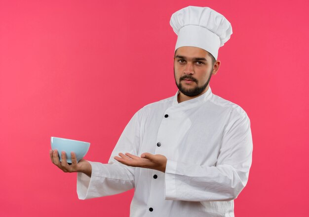 분홍색 공간에 고립 된 요리사 유니폼 들고 그릇에 젊은 남성 요리사