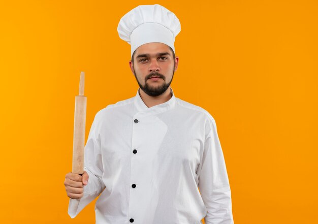 Free photo young male cook in chef uniform holding rolling pin looking  isolated on orange space