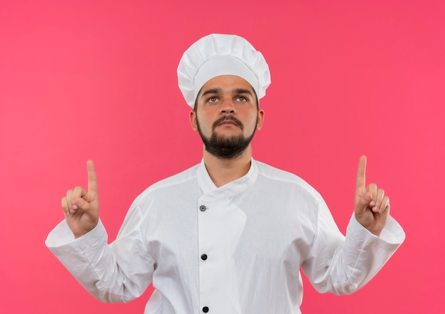 Free photo young male cook in chef uniform looking and pointing up isolated on pink space