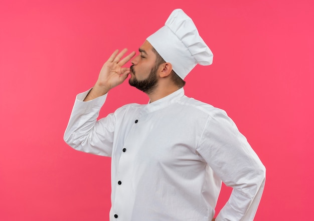 Young male cook in chef uniform looking at side doing tasty gesture