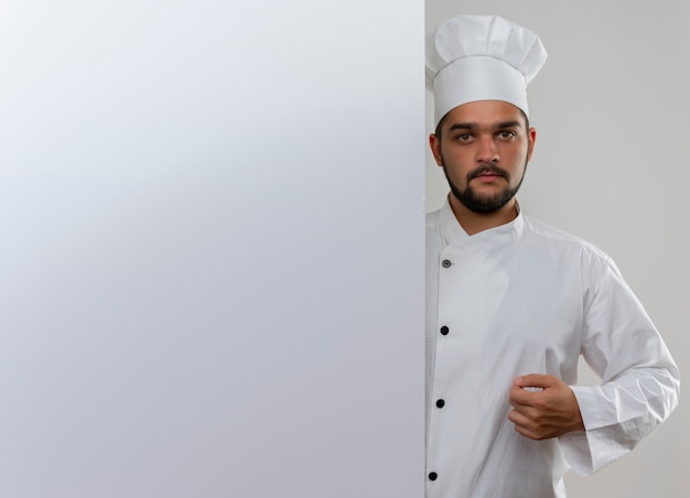 흰 벽보고 뒤에 서있는 요리사 유니폼에 젊은 남성 요리사