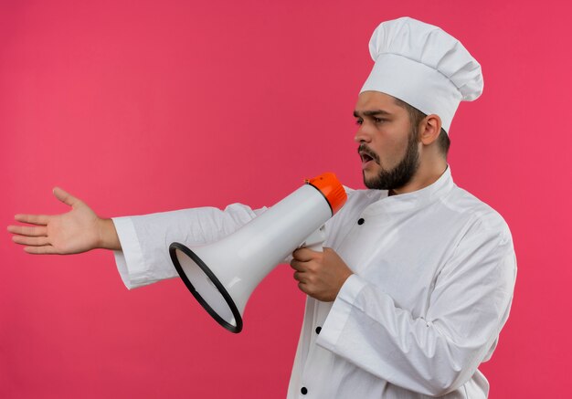 Young male cook in chef uniform talking by speaker stretching out hand and looking at side