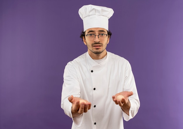 young male cook wearing chef uniform and glasses holding out eggs