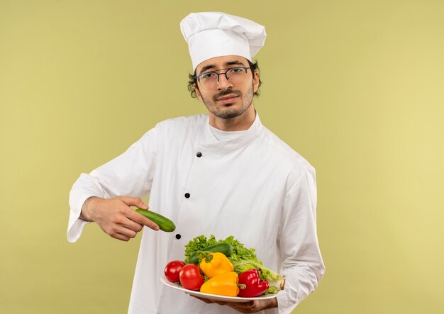 접시에 야채를 들고 요리사 유니폼과 안경을 착용하는 젊은 남성 요리사