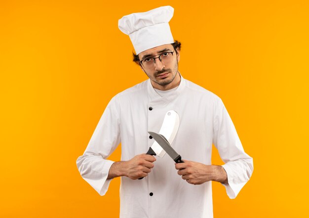 シェフの制服と眼鏡を身に着けている若い男性料理人は包丁とナイフを鋭くします