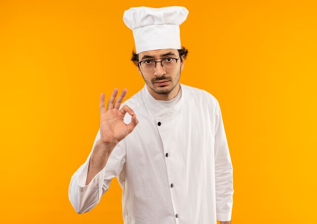 young male cook wearing chef uniform and glasses showing okey gesture 