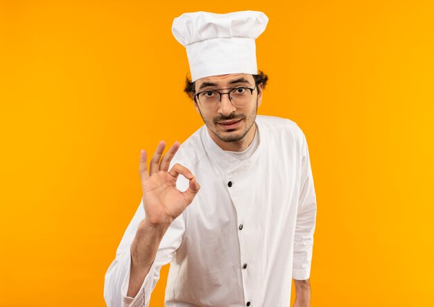 Young male cook wearing chef uniform and glasses showing okey gesture