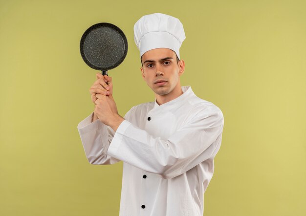  young male cook wearing chef uniform holding frying pan around shoulder on isolated green wall