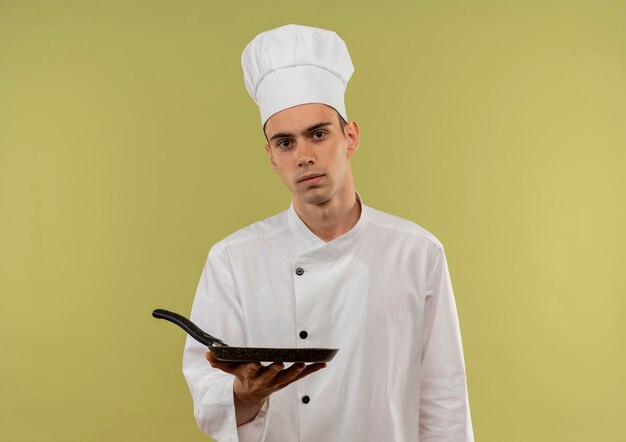  young male cook wearing chef uniform holding frying pan on isolated green wall