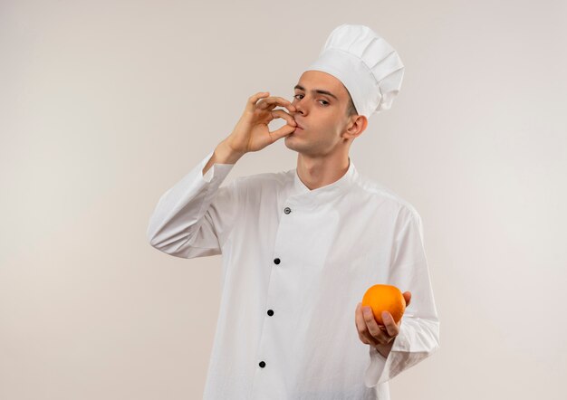  young male cook wearing chef uniform holding orange showing delicious gesture on isolated white wall with copy space