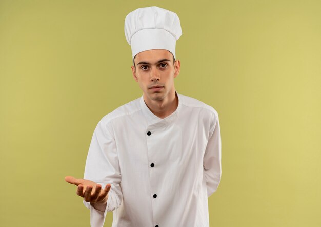  young male cook wearing chef uniform pretending holding something on isolated green wall with copy space