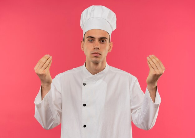 격리 된 분홍색 벽에 팁 제스처를 보여주는 요리사 유니폼을 입고 젊은 남성 요리사