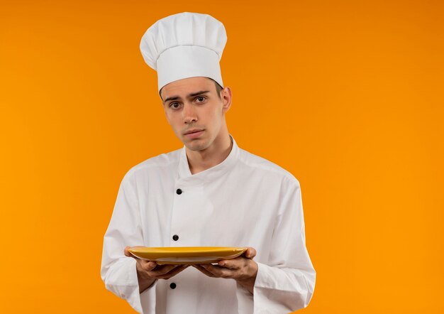  young male cool wearing chef uniform holding plate on isolated yellow wall with copy space