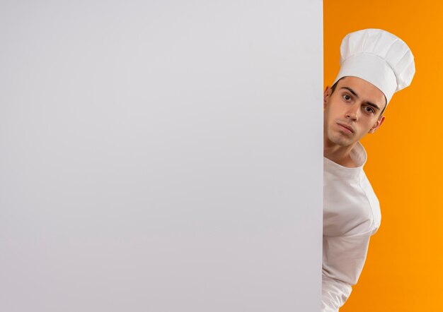  young male cool wearing chef uniform holding white wall on isolated yellow wall with copy space