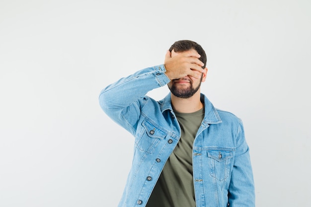 Young male covering eyes with hand in t-shirt jacket and looking excited 