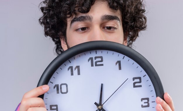 Young male curly hair isolated  colorful shirt hiding behind clock close-up